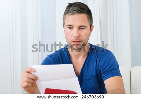 Portrait Of Unhappy Man Sitting On Sofa Reading Letter