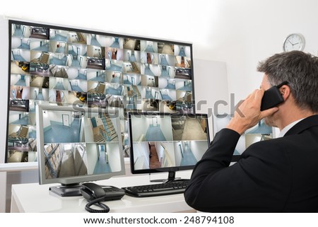 Security System Operator Looking At Cctv Footage While Talking On Telephone