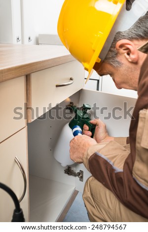 Pest Control Worker In Workwear With Flashlight And Spraying Pesticides Inside Cabinet
