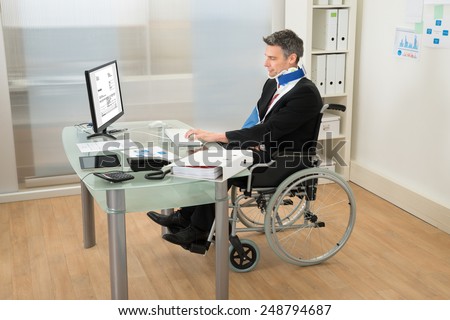 Disabled Businessman Sitting On Wheelchair Using Computer