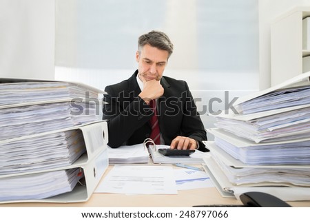 Photo Of Mature Businessman Calculating Invoices In Office