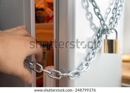 Close-up Of Person Trying To Open Fridge Locked With Chain And Padlock