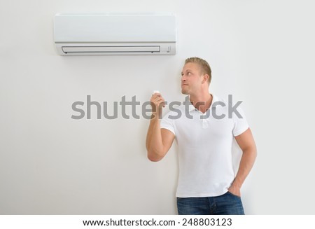 Portrait Of A Man Operating Air Conditioner With Remote Controller