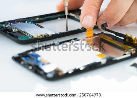 Close-up Of Human Hand Repairing Cellphone With Screwdriver On Desk