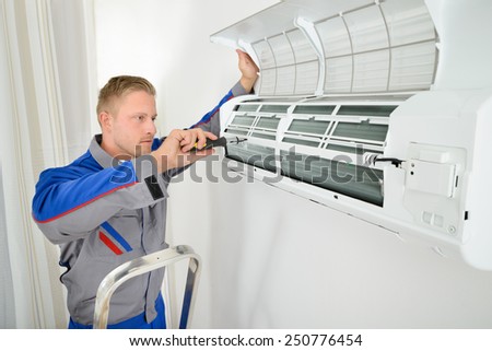 Portrait Of Male Electrician Repairing Air Conditioner Standing On Stepladder
