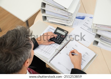 High Angle View Of Businessman Calculating Invoices At Office