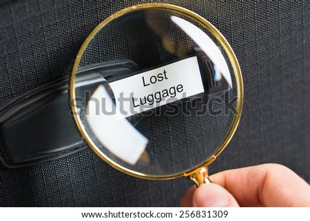 Hand Holding Magnifying Glass On Travel Bag With A Lost Luggage Label