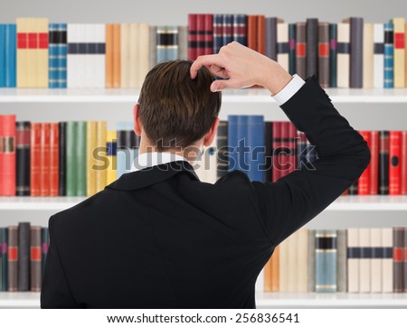 Rear View Of Man In A Suit Scratching His Head In Library