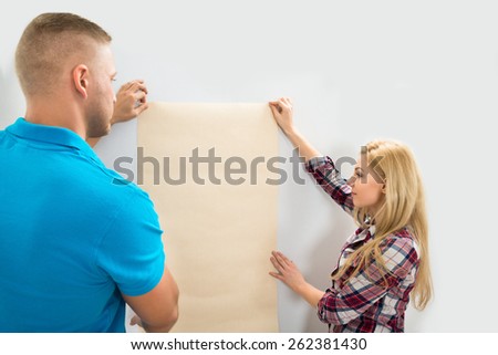 Portrait Of Young Couple Applying Wallpaper On Wall In New Home