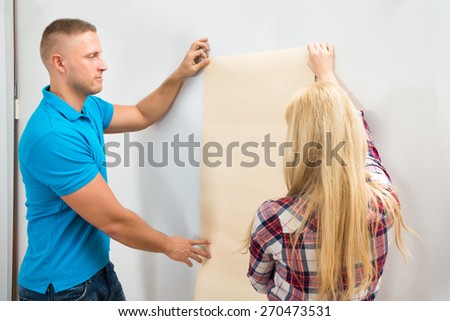 Portrait Of Young Couple Applying Wallpaper On Wall In New Home