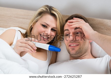 Couple Looking At A Positive Pregnancy Test In Bedroom