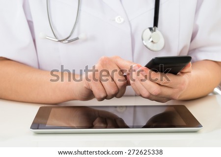 Close-up Of Doctor Using Mobile Phone With Digital Tablet At Desk