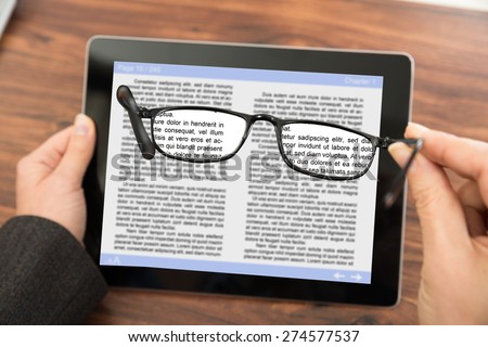 Close-up Of Person Reading E-book On Digital Tablet With Spectacles
