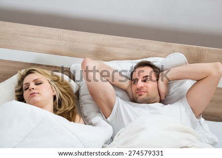 Man Covering Ears While Woman Sleeping In Bedroom At Home