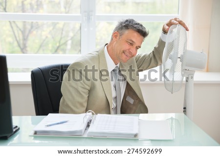 Portrait Of A Happy Businessman Sitting Near Fan In Office
