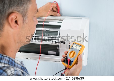 Portrait Of A Mid-adult Male Technician Testing Air Conditioner With Digital Multimeter