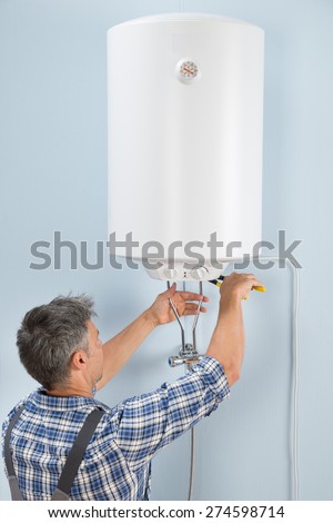 Portrait Of Happy Male Plumber Repairing Electric Boiler