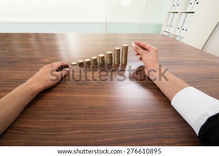 Businessperson Hand Putting Coin To Stack Of Coins At Desk