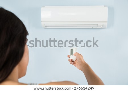 Close-up Of Young Woman Operating Air Conditioner With Remote Control