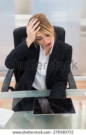 Shocked Businesswoman Looking At Broken Screen Digital Tablet On Desk