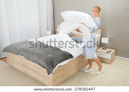 Happy Female Housekeeping Worker With Pillows In Hotel Room