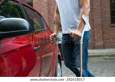 Close-up Of A Disabled Man With Crutches Opening Door Of A Car