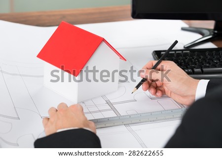 Close-up Of Architect With House Model Making Blueprint