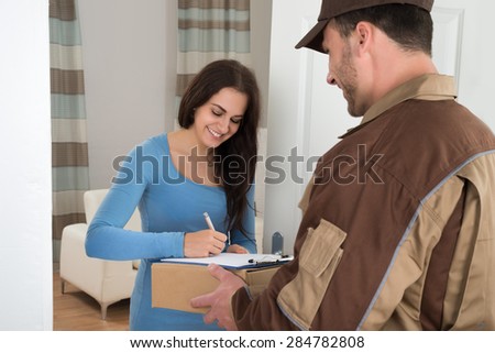 Young Woman Signing While Receiving Courier From Delivery Man At Home