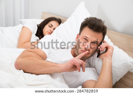 Man Talking Privately On Cellphone While His Wife Sleeping On Bed