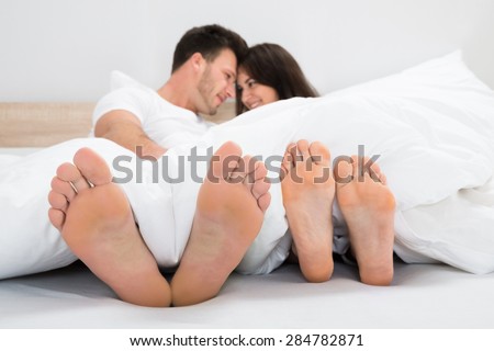Romantic Smiling Couple With Bare Feet On Bed