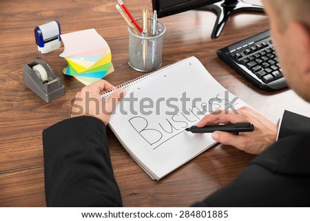 Close-up Of Businessman Writing The Text Business On Notebook In Office