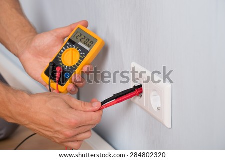 Close-up Of Person Hand Metering Socket Voltage With Digital Multimeter