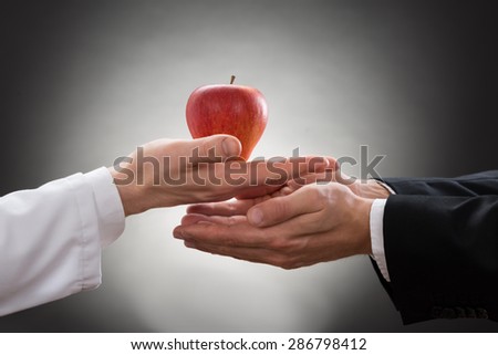 Close-up Of A Doctor\'s Hand Offering Apple To Another Person