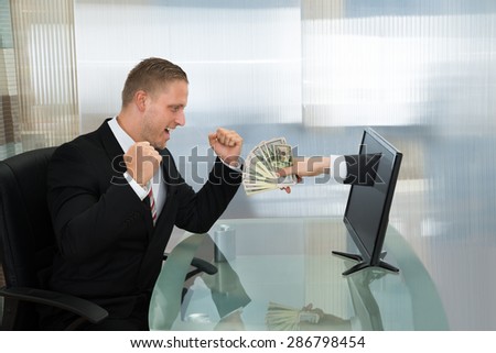 Excited Young Businessman Looking At Money Coming Out From Computer Flat Screen