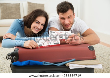 Portrait Of Happy Young Couple Packing Luggage Showing Boarding Pass