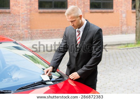 Portrait Of A Man Removing Parking Ticket On Car Windscreen