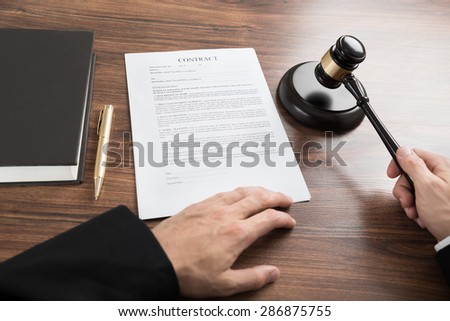 Close-up Of Judge Hitting The Gavel With Contract Paper At Desk
