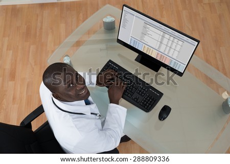 High Angle View Of Happy Young African Male Doctor Typing On Computer Keyboard