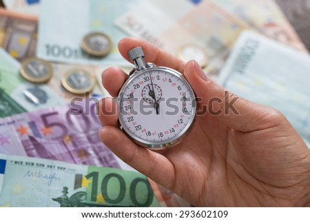 Close-up Of Person Hands Holding Stopwatch Over Money Background