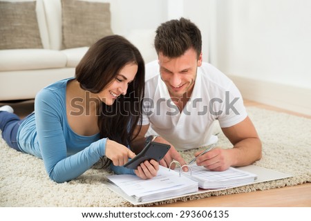 Portrait Of A Happy Young Couple Lying On Rug Calculating Invoice