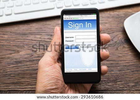 Close-up Of Person Hands With Mobile Phone Showing Signing App At Wooden Desk