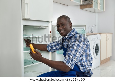 Happy African Technician Repairing Refrigerator Appliance In Kitchen Room