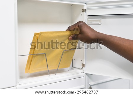 Close-up Of Person Hands Holding Envelope In Mailbox