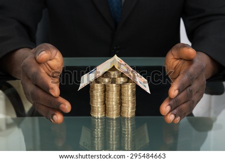Close-up Of Businessman Hands Protecting House Made Of Money