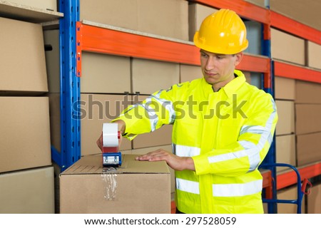 Young Worker Packing Cardboard Box With Tape Gun Dispenser In Warehouse