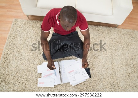 Portrait Of Young African Man Sitting On Carpet Calculating Invoices Using Calculator