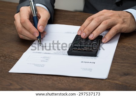Close-up Of Businessperson Checking Invoice With Calculator