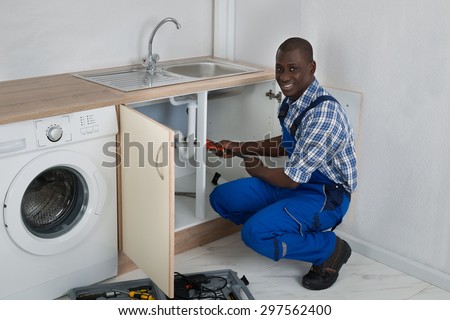 Young Happy African Male Plumber Fixing Sink In Kitchen