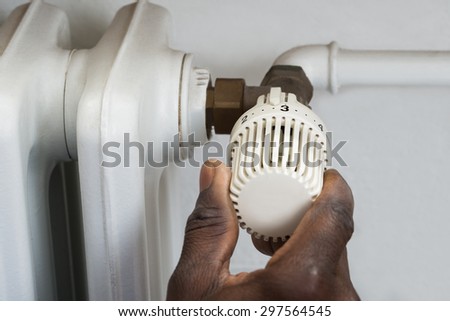 Close-up Of Person Hands Adjusting Thermostat Radiator Valve