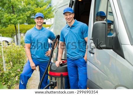 Two Happy Male Cleaners Standing With Vacuum Cleaner Near The Van